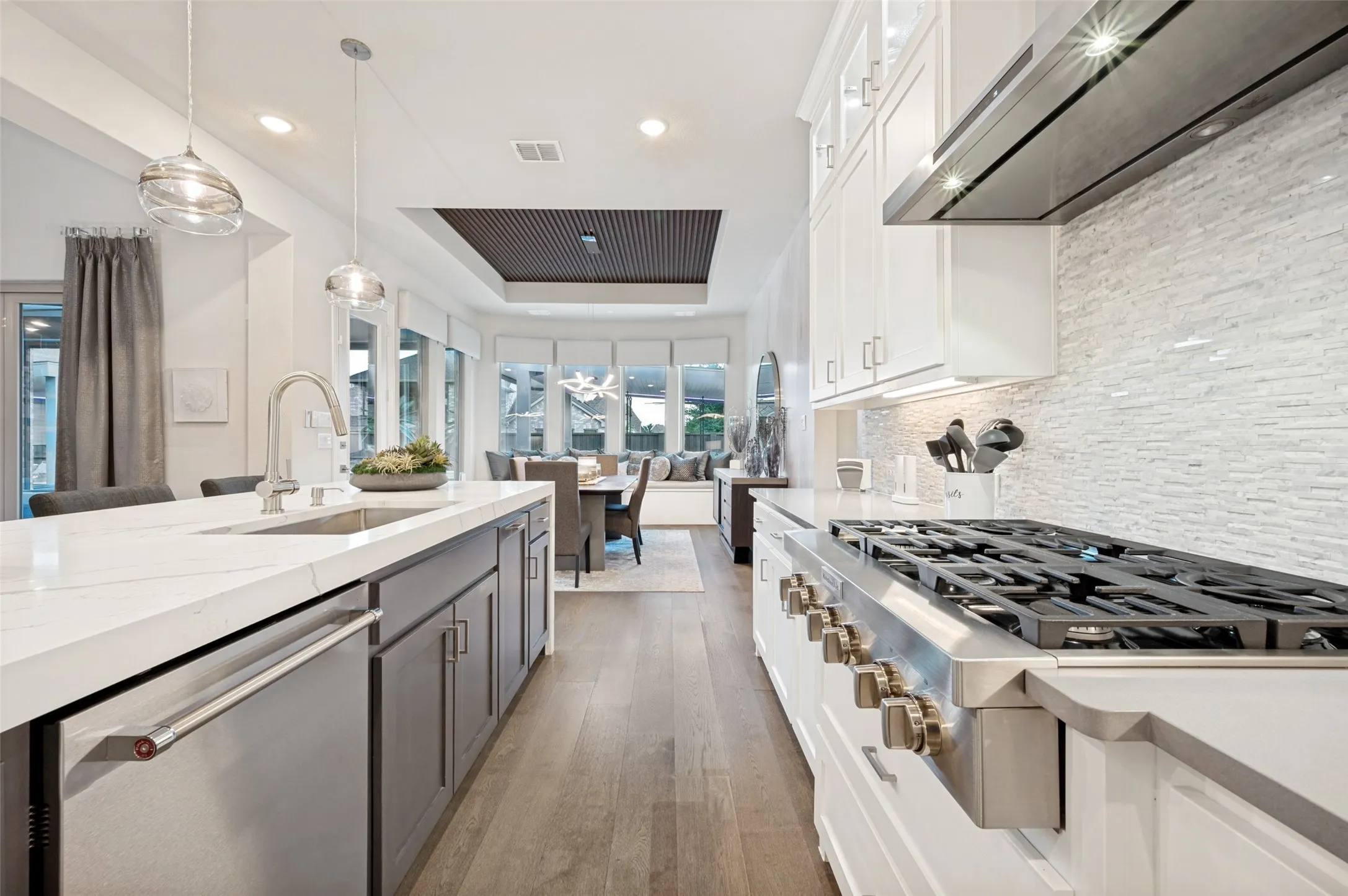 Kitchen featuring a large central island with an undermount sink, a gas range with a stainless steel hood, white cabinetry, and wood-finish flooring