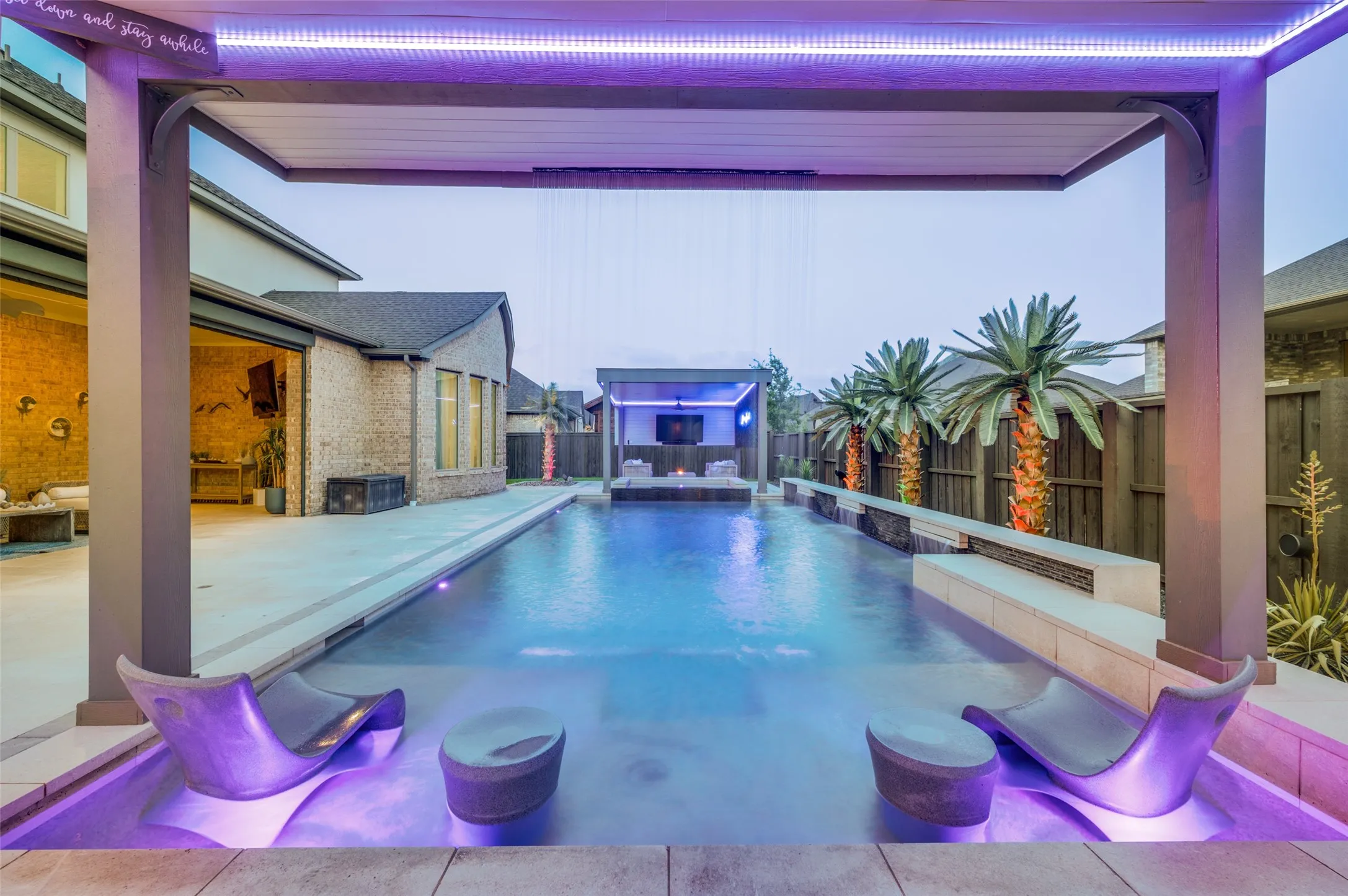 Expansive outdoor living area featuring a rectangular pool, integrated water features, and a covered patio structure
