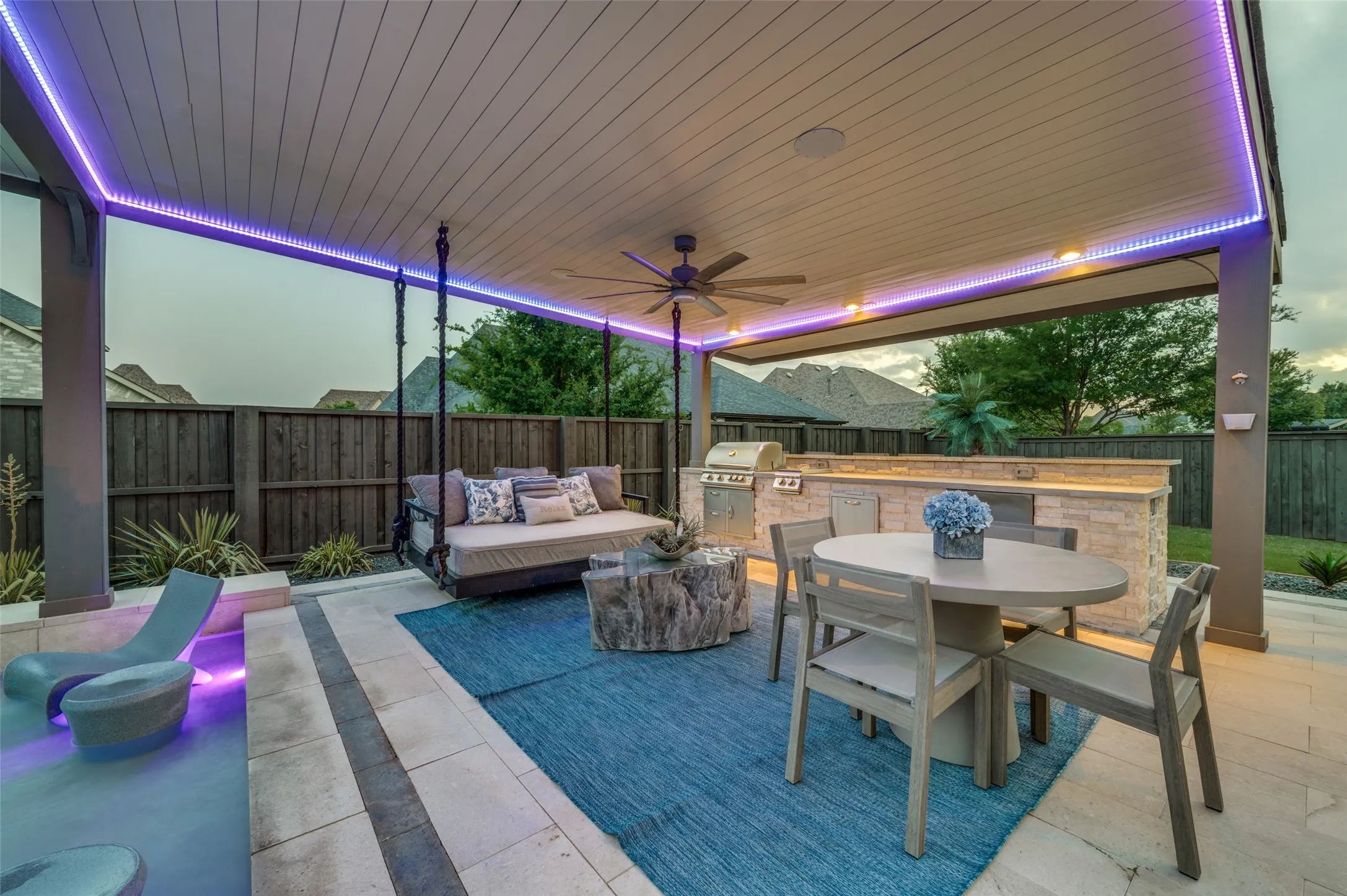 Covered patio with integrated ambient lighting, ceiling fan, and outdoor kitchen featuring a built-in grill and stone-clad base