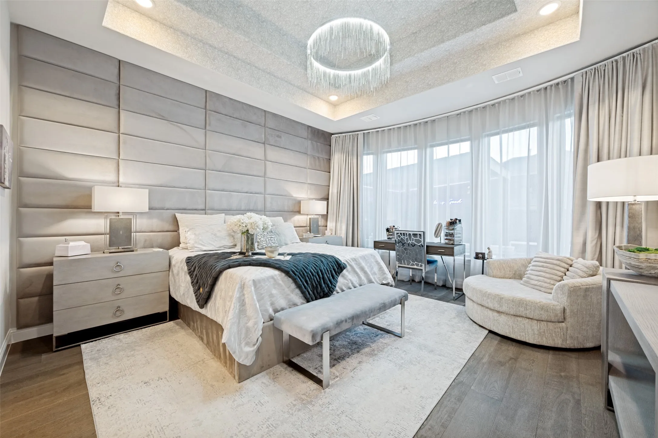 Tray ceiling with recessed lighting, wood-finish flooring, padded accent wall, and curved window wall with sheer and blackout drapery