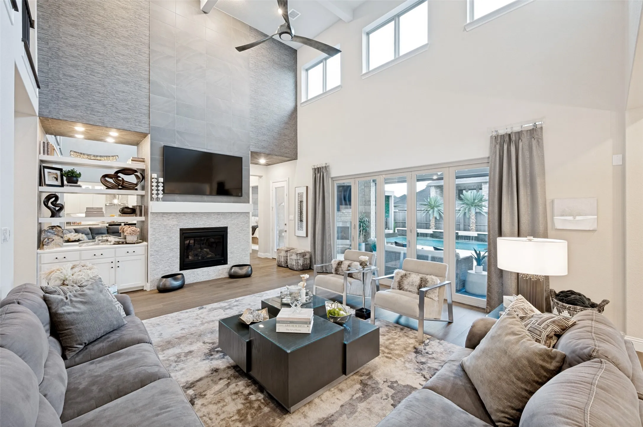 Vaulted ceiling with transom windows, built-in shelving, stone-clad fireplace with mantel, wood-finish flooring, and multi-panel sliding glass doors