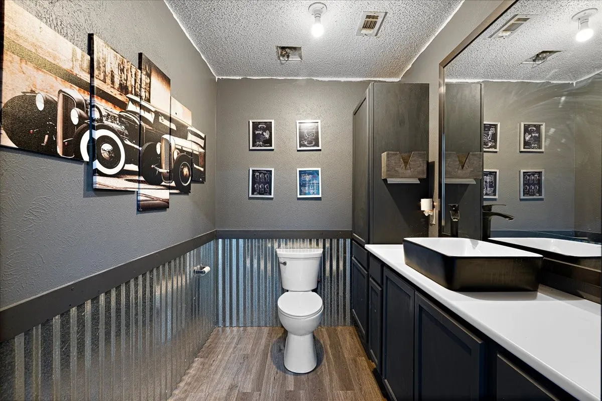 Corrugated metal wainscoting, wood-finish flooring, white countertop, black vessel sink, and matte black faucet