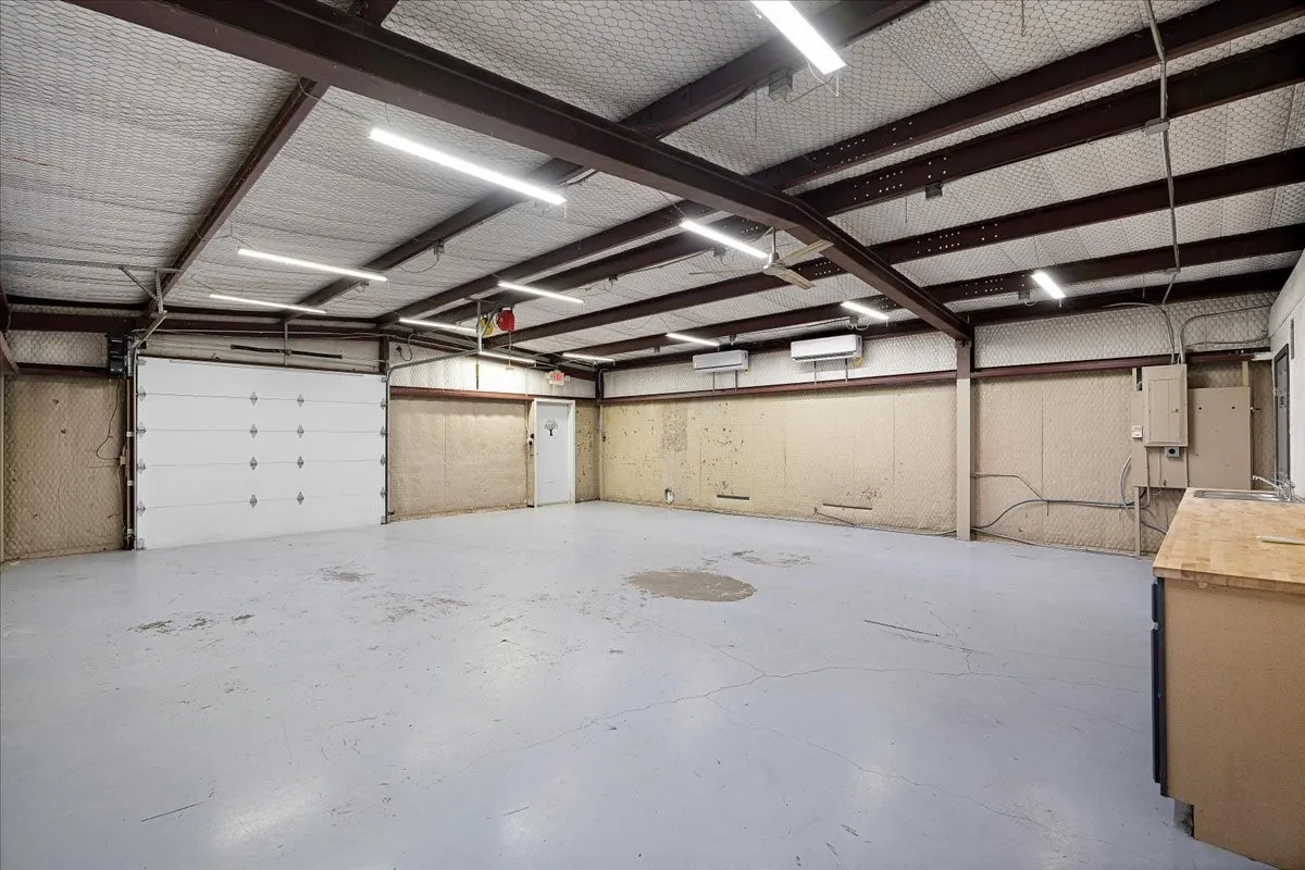Spacious interior featuring a roll-up garage door, painted concrete flooring, exposed ceiling beams, and integrated lighting