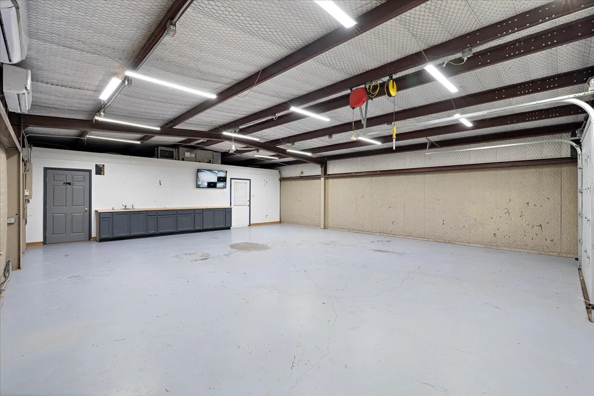 Spacious interior with high ceilings, multiple linear fluorescent light fixtures, built-in cabinetry with wood-finish countertops, and an overhead door