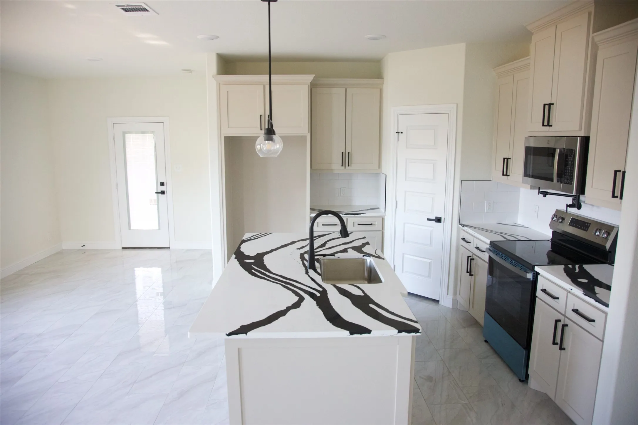 Contemporary kitchen featuring a center island with an undermount sink, white cabinetry with dark hardware, a stainless steel microwave, and a black cooktop
