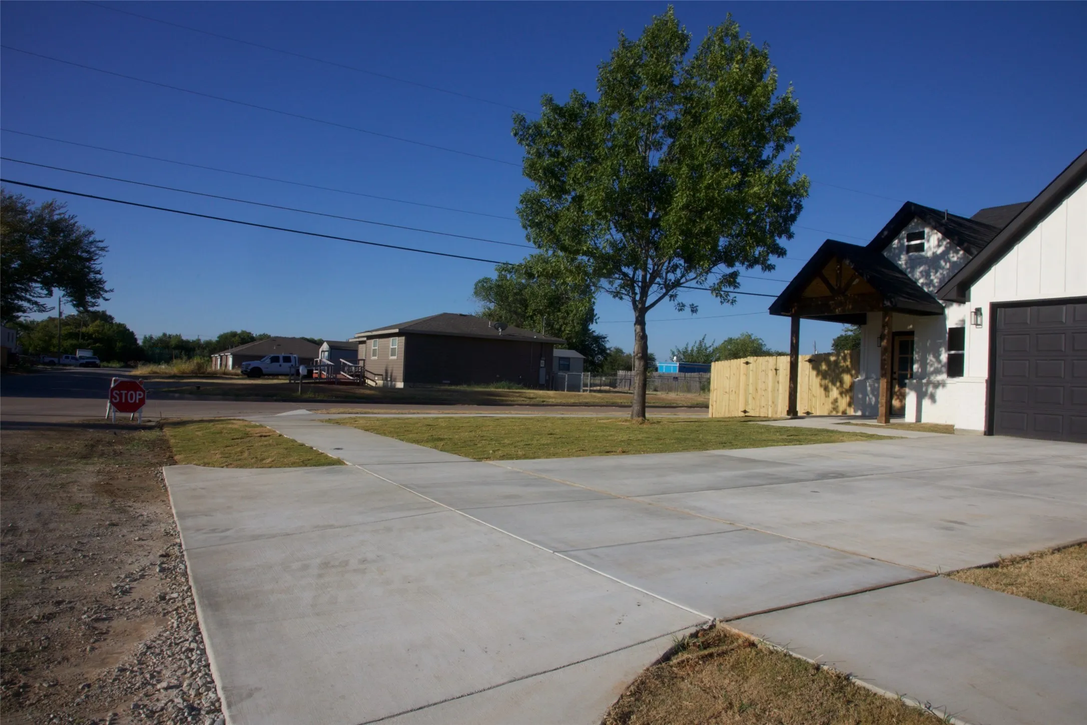 Expansive concrete driveway, attached garage with a dark panel door, white exterior siding, covered entry porch with exposed wood beams, and a mature tree