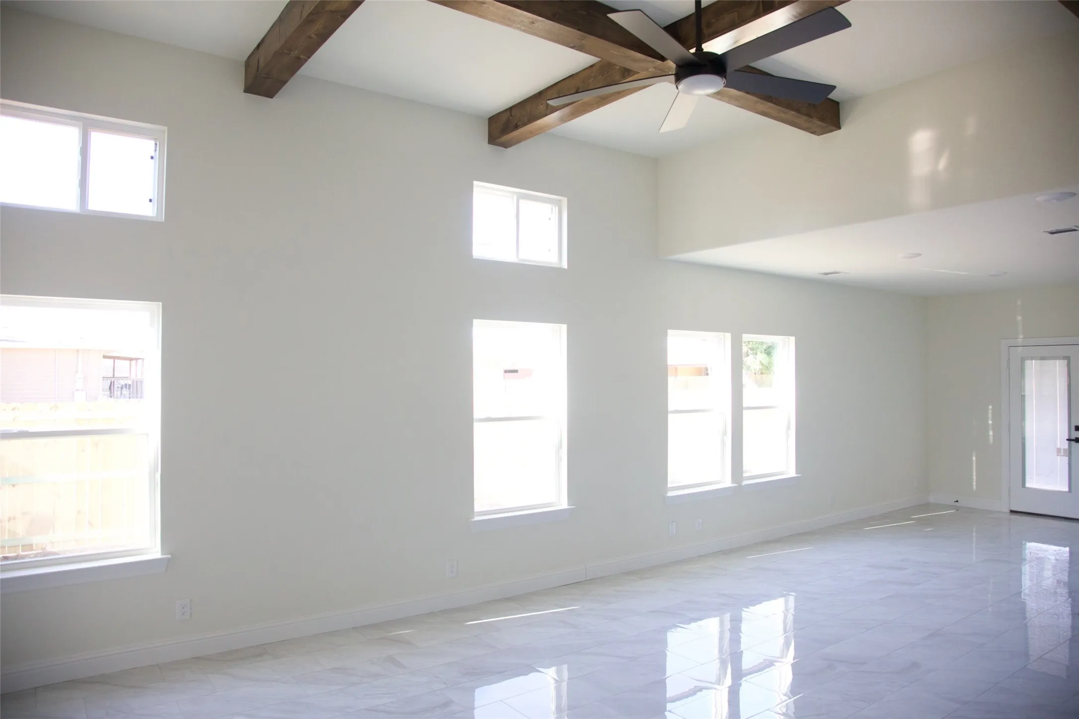 Vaulted ceiling with exposed wood beams, high windows, white walls, and a multi-blade ceiling fan
