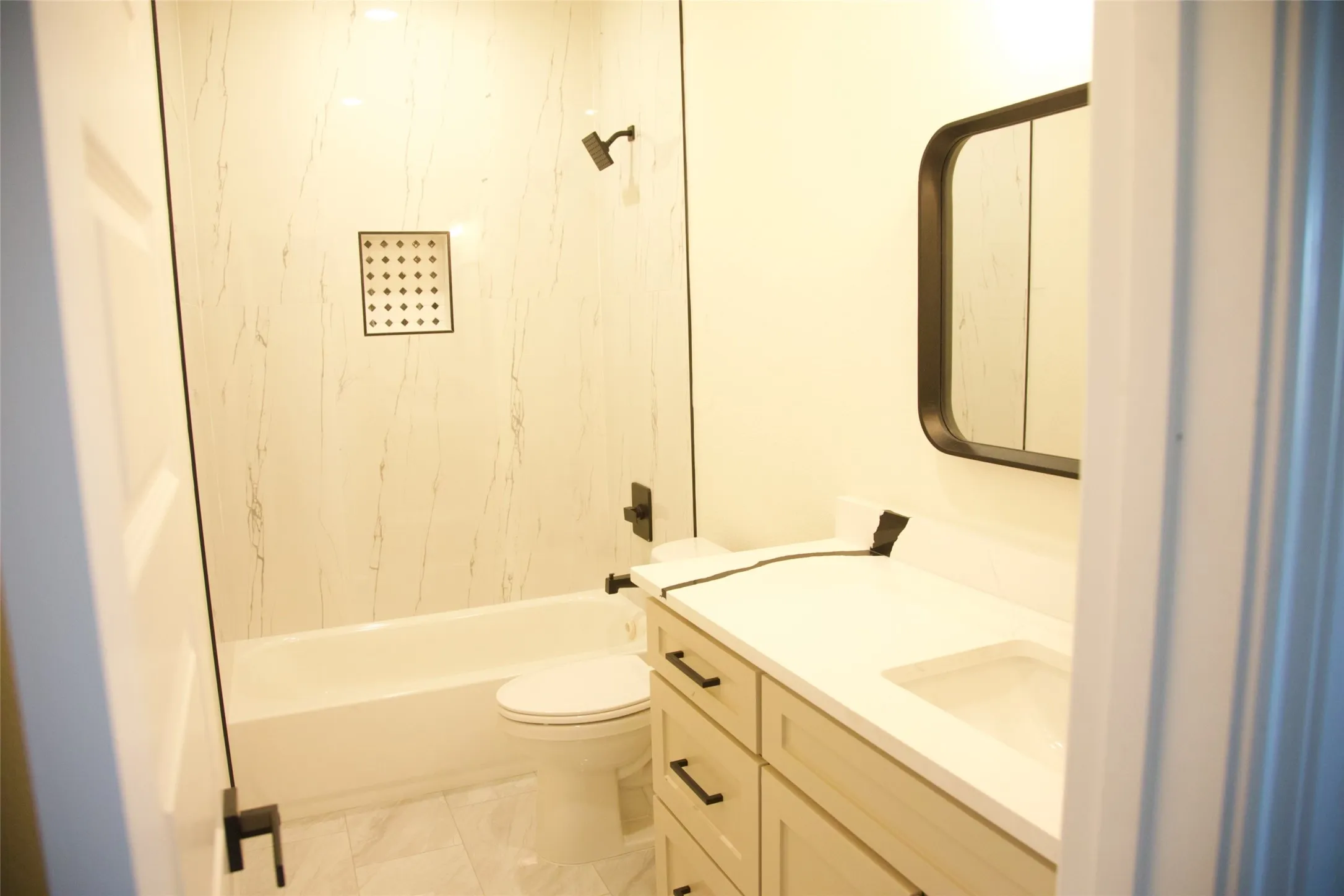 Bathroom featuring a built-in tub with a shower, white paneled surround, and a recessed shower niche