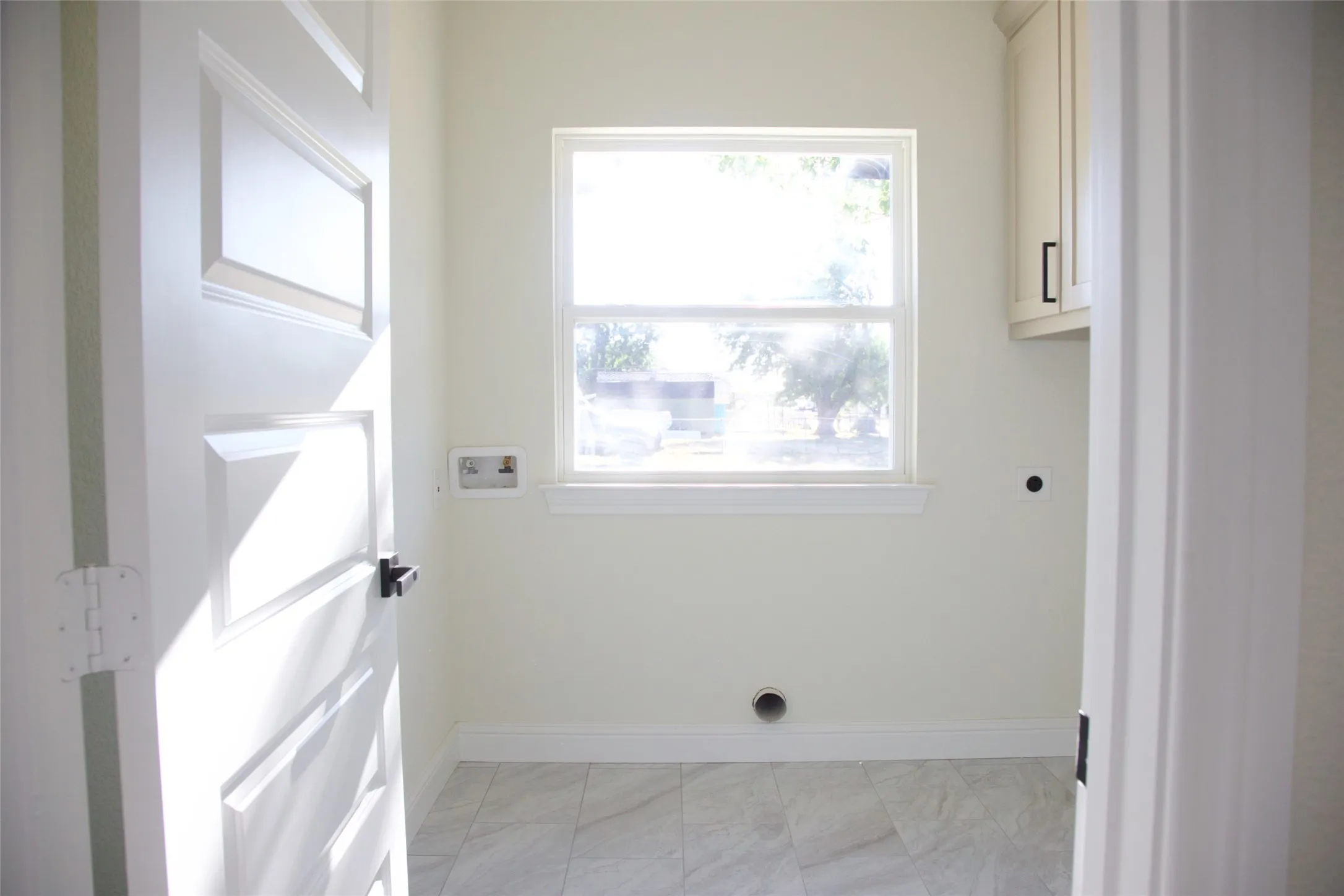 Recessed window with white trim, upper cabinetry featuring black hardware, white paneled door with black hardware, and tiled flooring