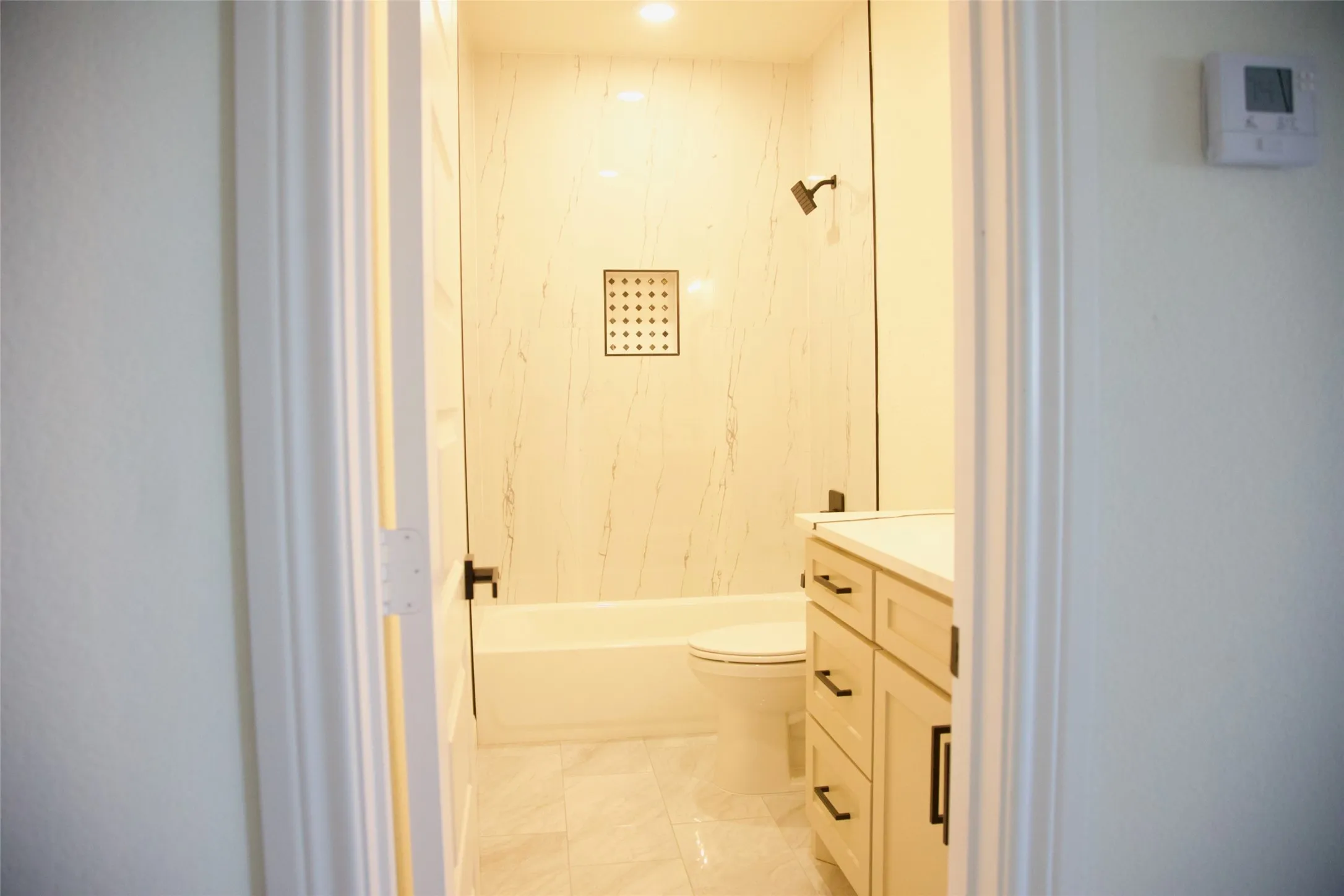 Bathroom featuring a full tub with shower, integrated shower niche, glass shower partition, single vanity, and tiled flooring