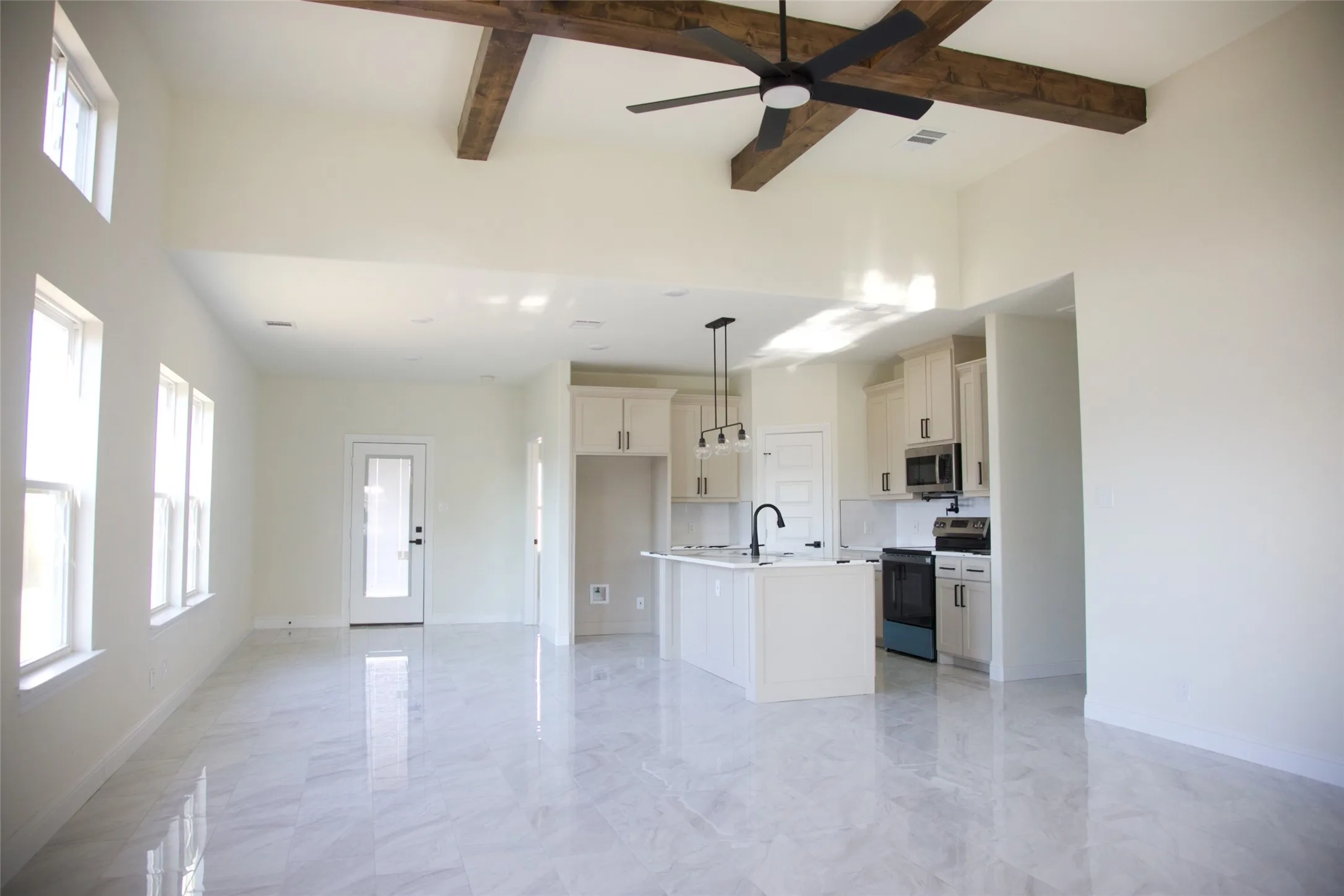 Open-concept living space featuring high ceilings with exposed beams, an integrated kitchen with a central island, and modern pendant lighting