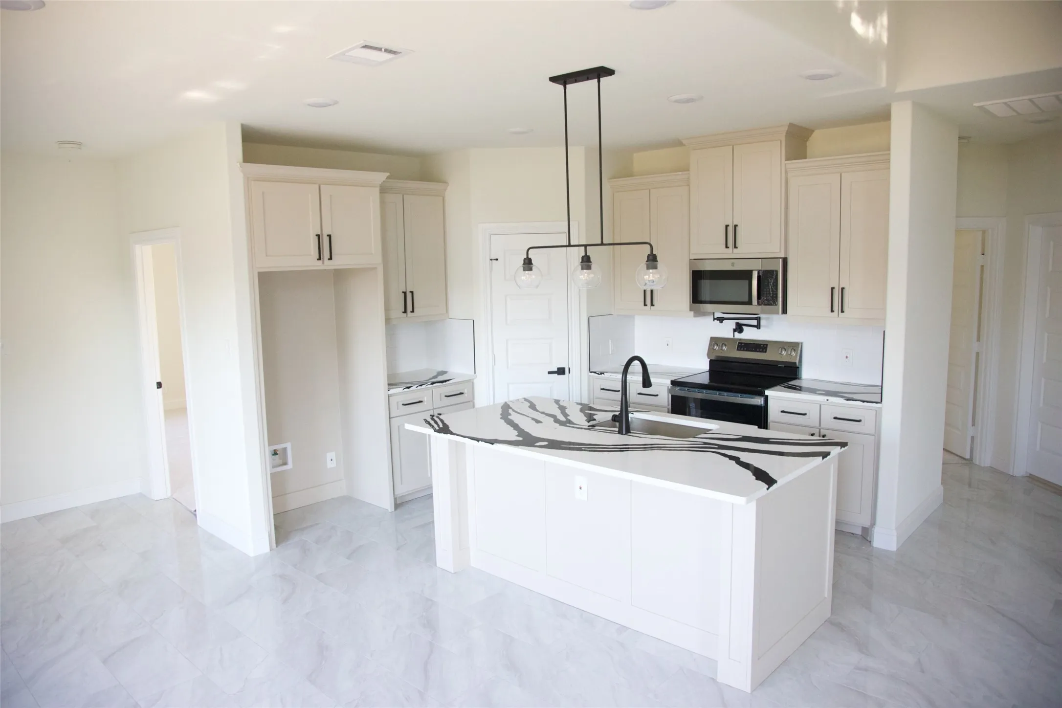 Contemporary kitchen featuring a center island with a large sink and faucet, white cabinetry with dark hardware, stainless steel microwave, and integrated cooktop