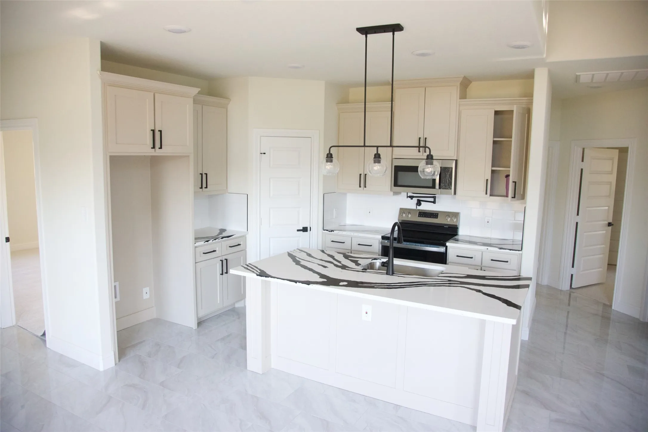 Kitchen featuring a central island with a large countertop, white cabinetry with black hardware, stainless steel appliances, and light-toned flooring