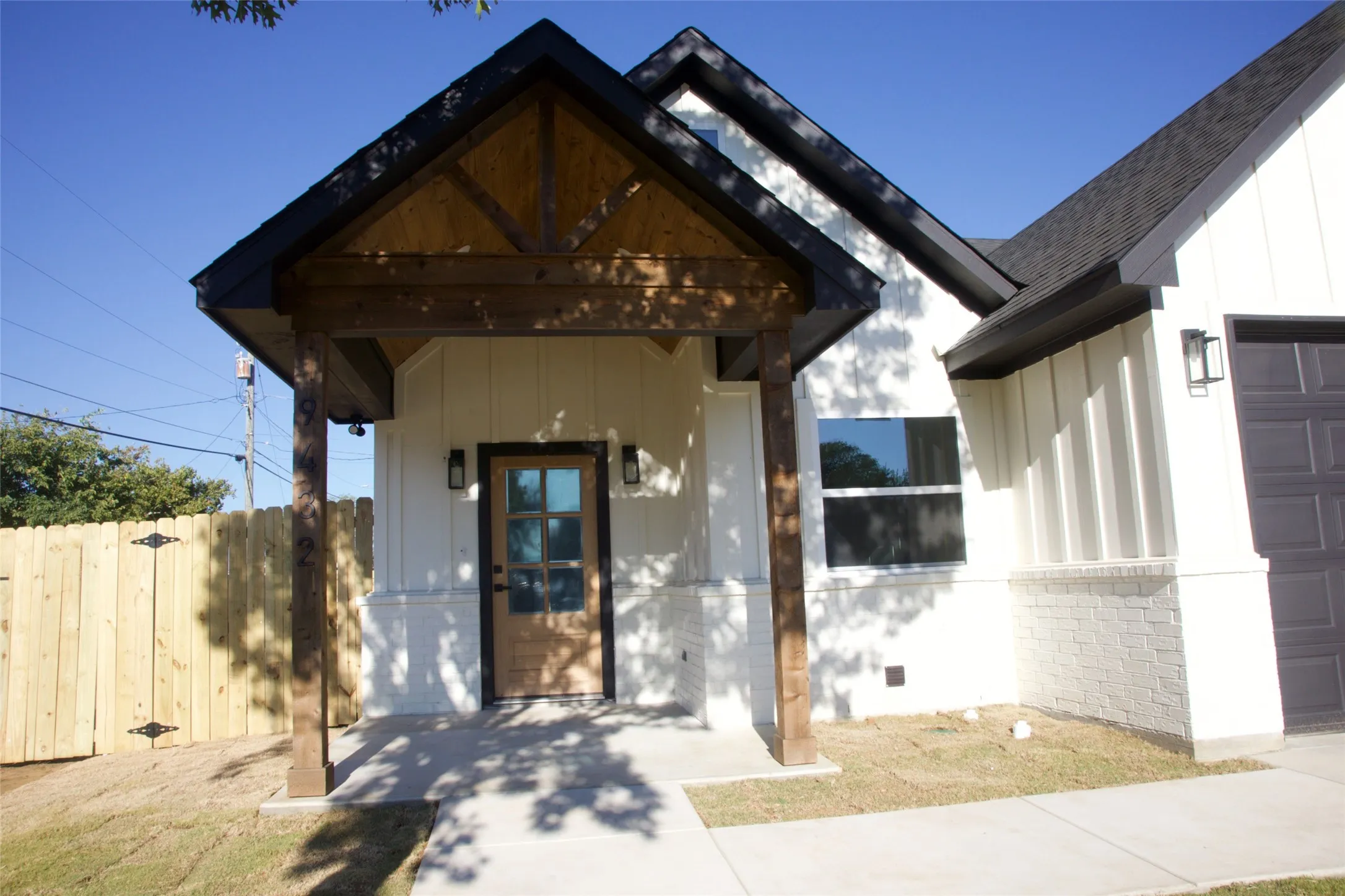 Contemporary exterior featuring white board and batten siding, dark shingle roof, and a wood-finish entry door with multiple glass panes