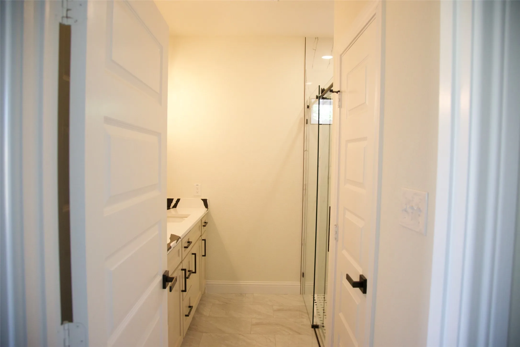 White panel doors with dark hardware, a vanity with a white countertop, and glass shower enclosure