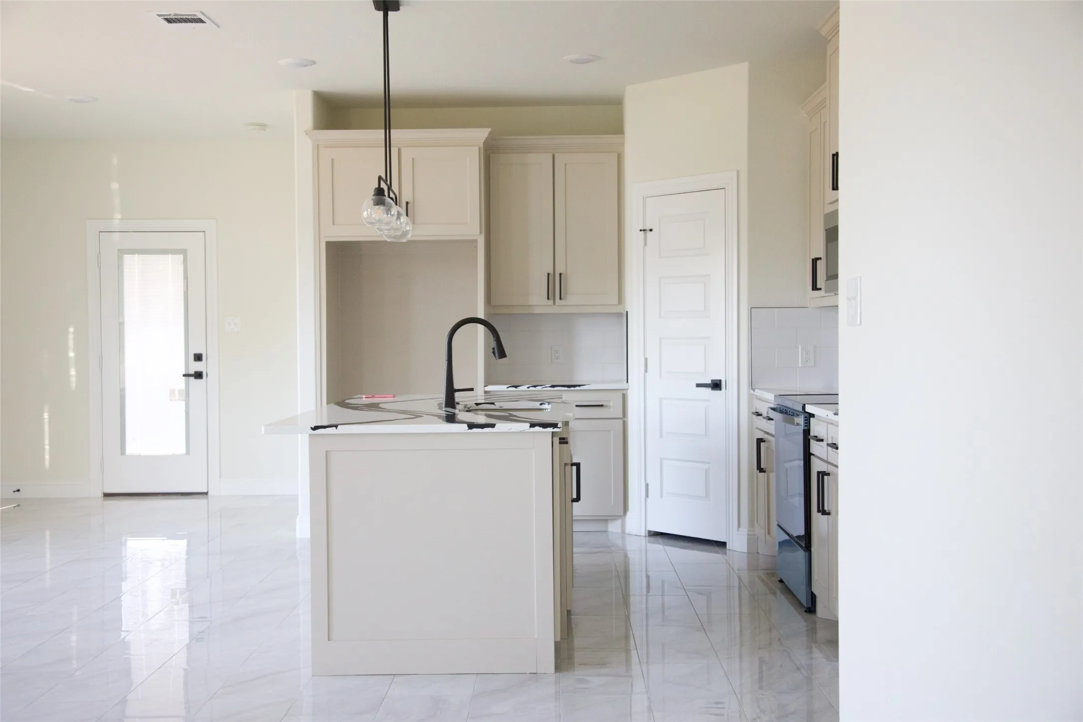 Kitchen featuring an island with a built-in sink and matte black faucet, white cabinetry with black hardware, and an electric range