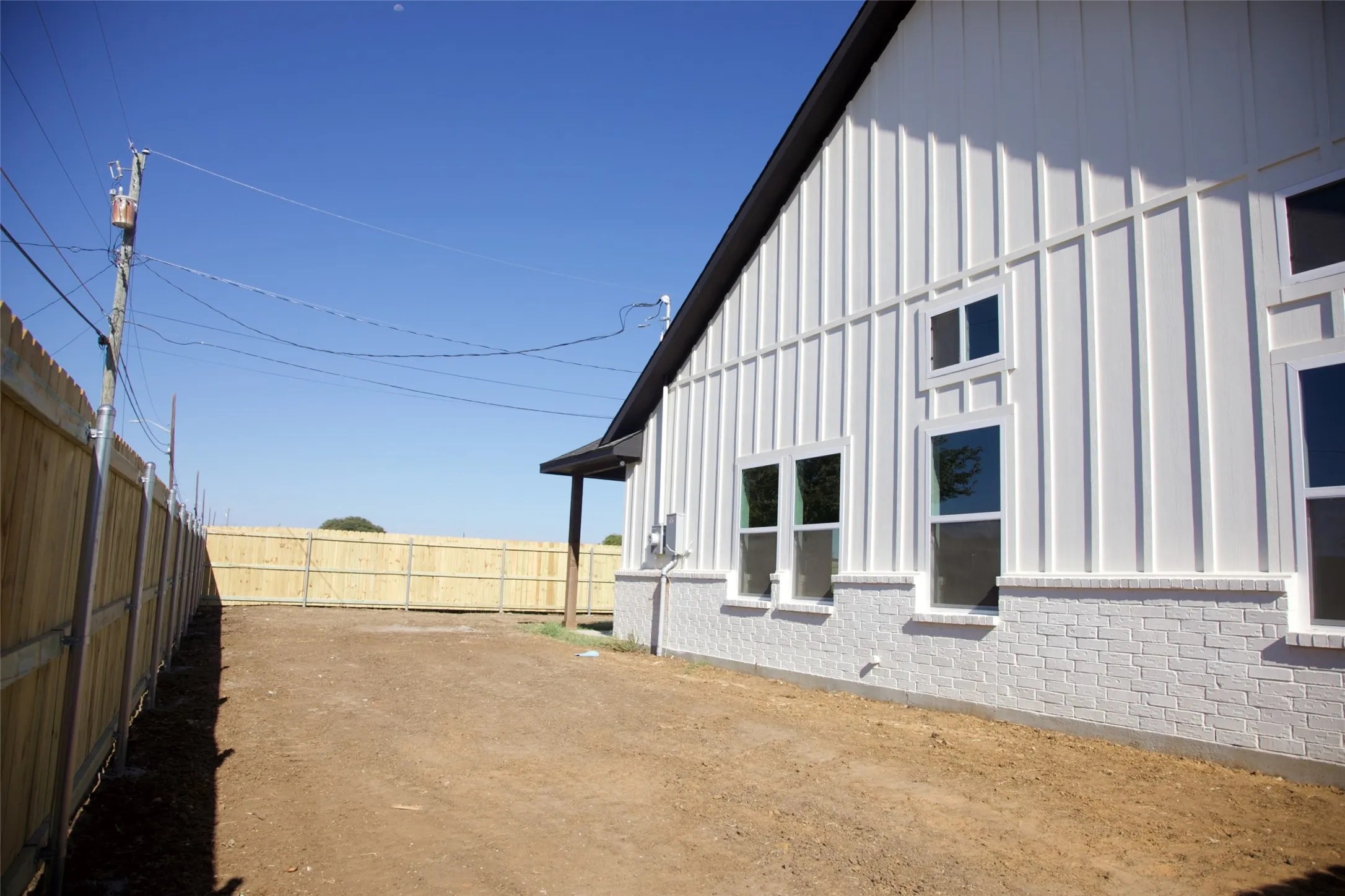 White board and batten siding with contrasting dark trim, white brick foundation, multiple windows with white frames, and a wooden privacy fence