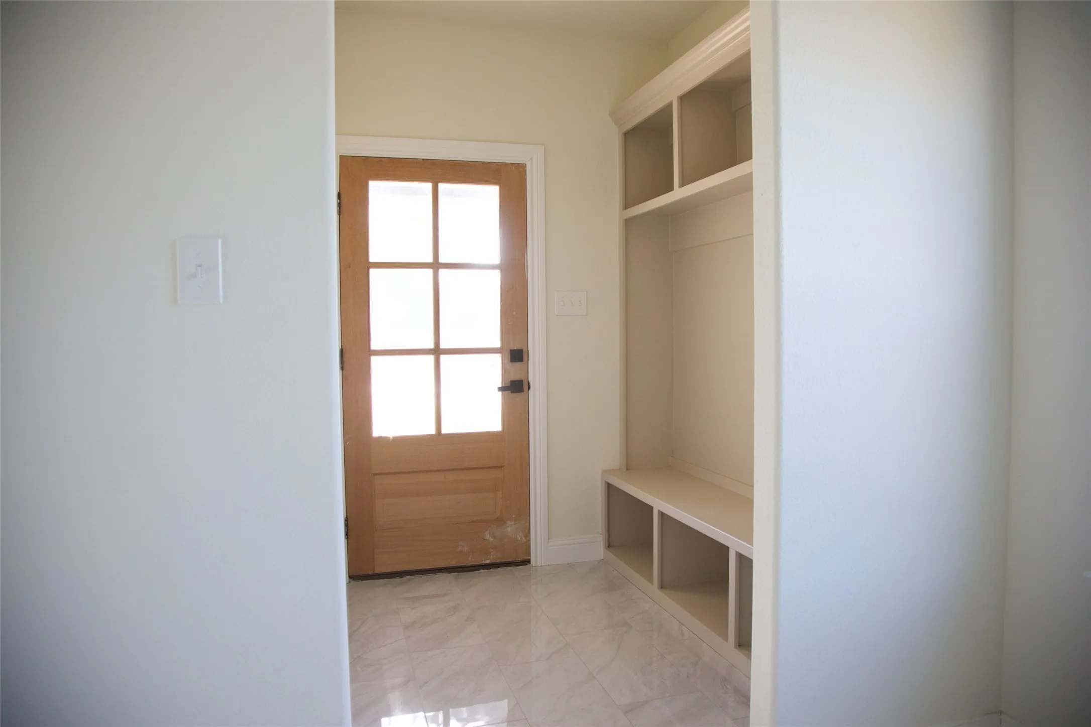 Wood-paneled entry door with glass inserts, built-in storage bench with cubbies, and marble-finish tile flooring
