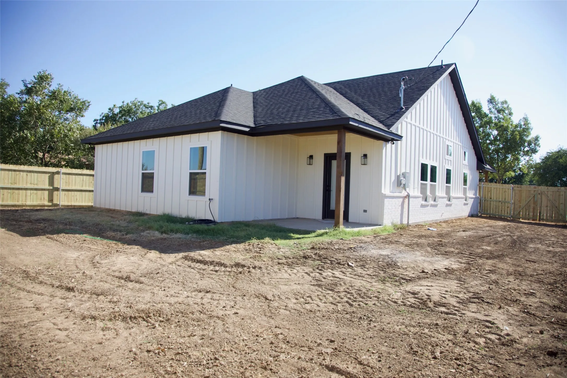 Exterior featuring white board and batten siding, dark shingle roof, dark trim, and a covered porch