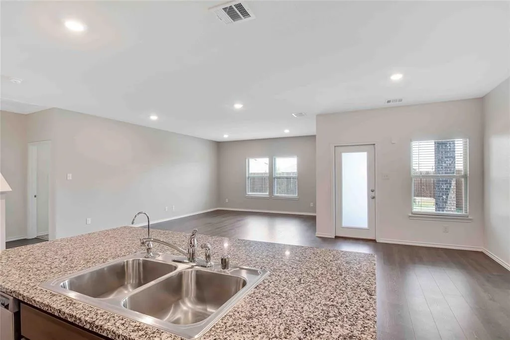 Kitchen with a kitchen island with sink, light stone countertops, sink, and dark wood-type flooring