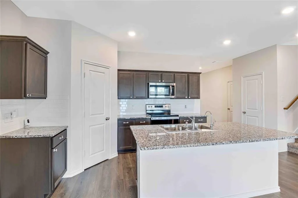 Kitchen with dark hardwood / wood-style floors, a center island with sink, stainless steel appliances, and sink