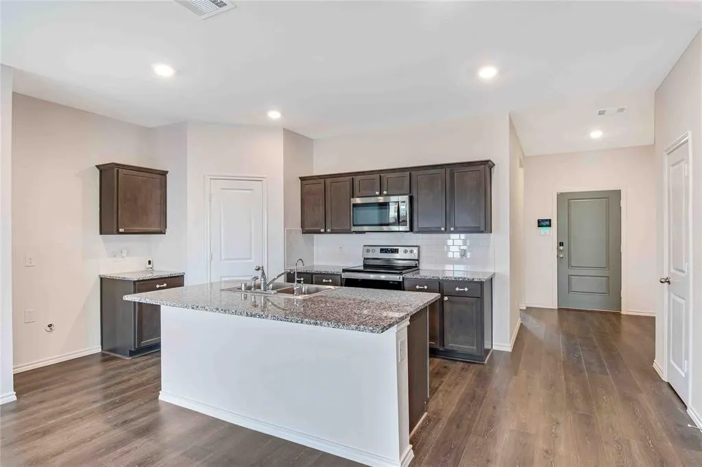 Kitchen featuring dark brown cabinets, an island with sink, dark wood-type flooring, sink, and stainless steel appliances