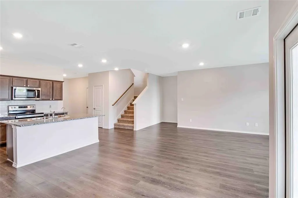 Kitchen featuring dark hardwood / wood-style floors, light stone countertops, stainless steel appliances, and a center island with sink
