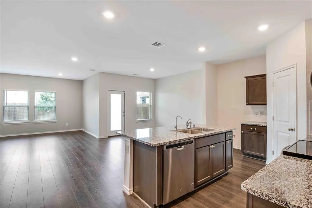 Kitchen with a center island with sink, light stone counters, dishwasher, dark wood-type flooring, and sink