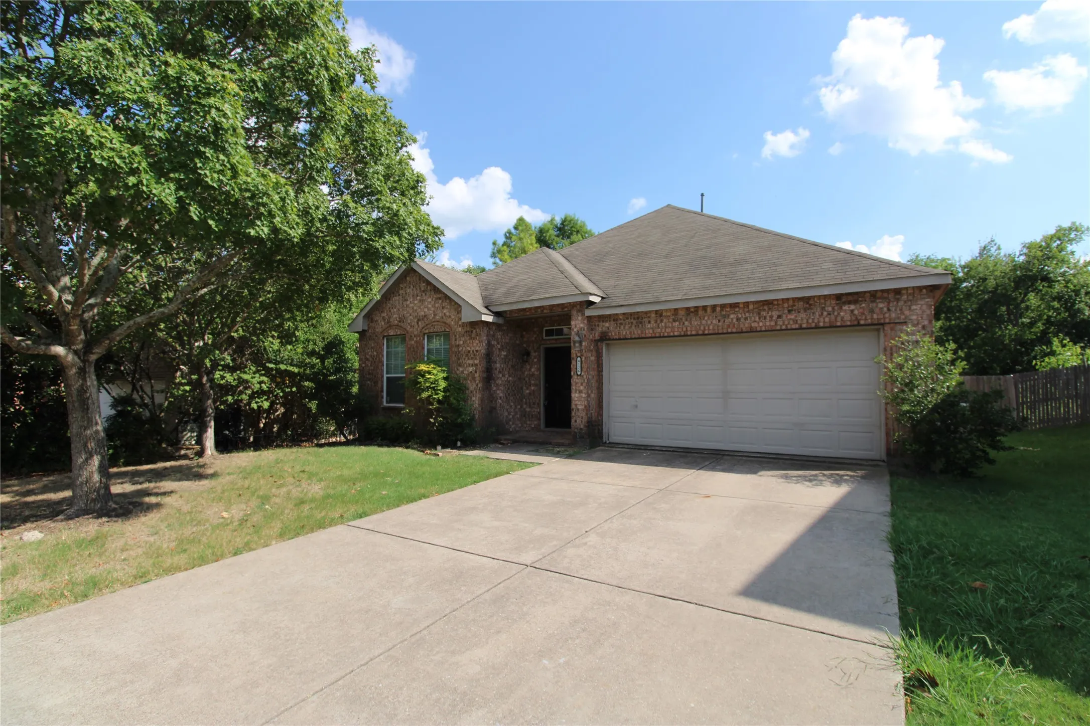 Brick exterior with an attached garage, concrete driveway, and mature landscaping