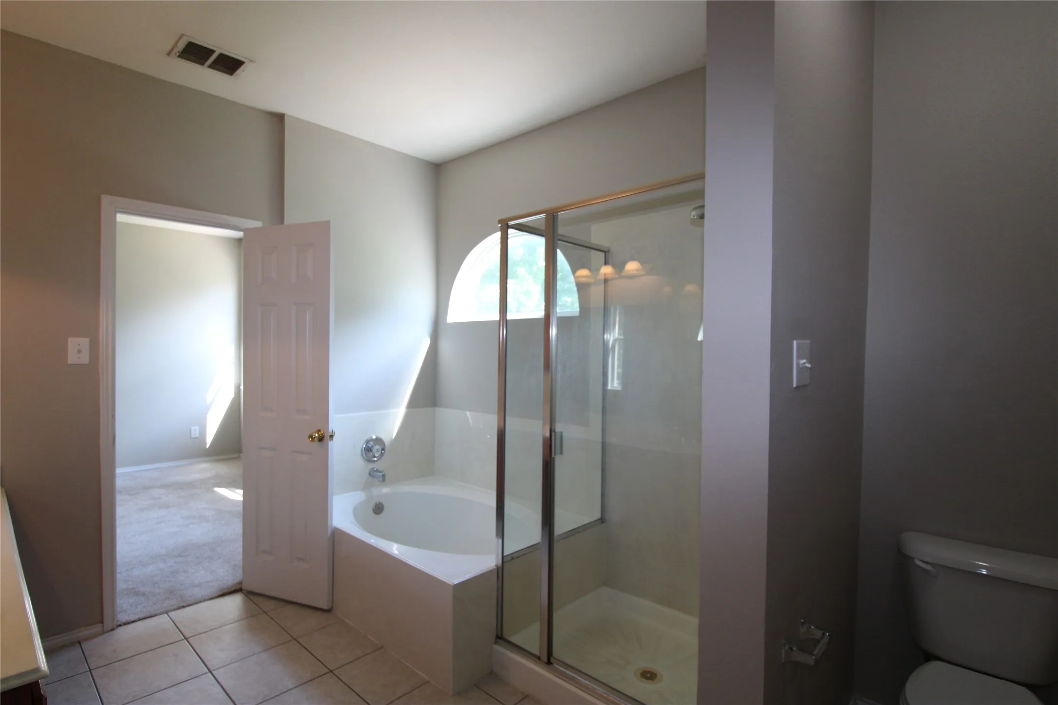 Step-in shower with clear glass enclosure and chrome hardware, tiled flooring, built-in soaking tub, and a toilet