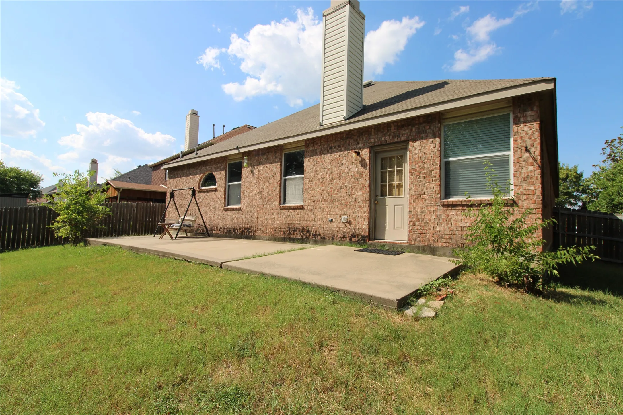 Brick exterior, rear patio, fenced backyard, exterior door, and chimney