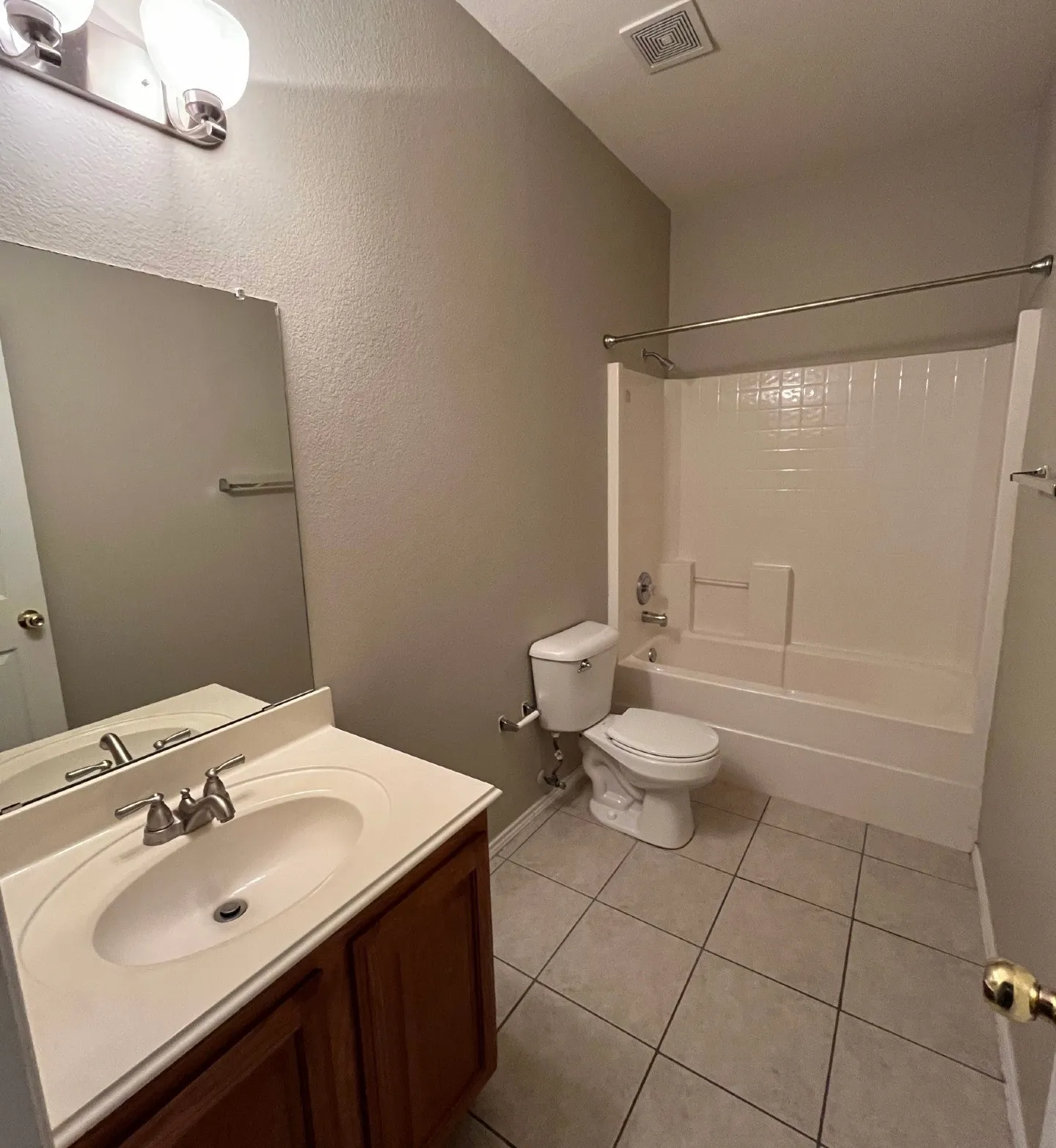 Full bathroom featuring a single vanity with wood-finish cabinetry, a built-in tub with shower, and tile flooring
