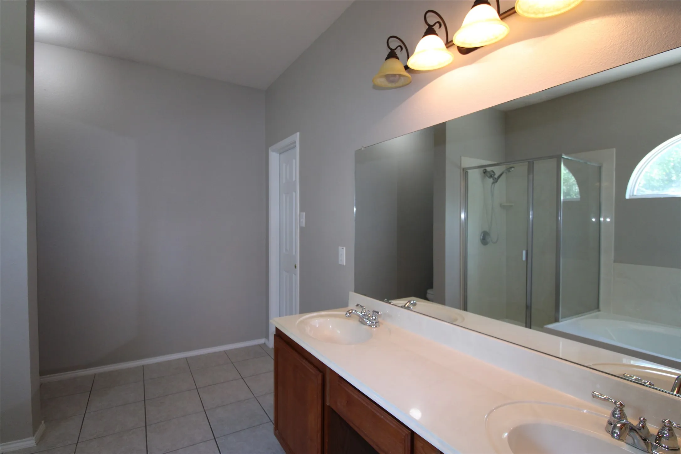 Dual vanity with integrated sinks, full-width mirror, tile flooring, and a glass-enclosed shower