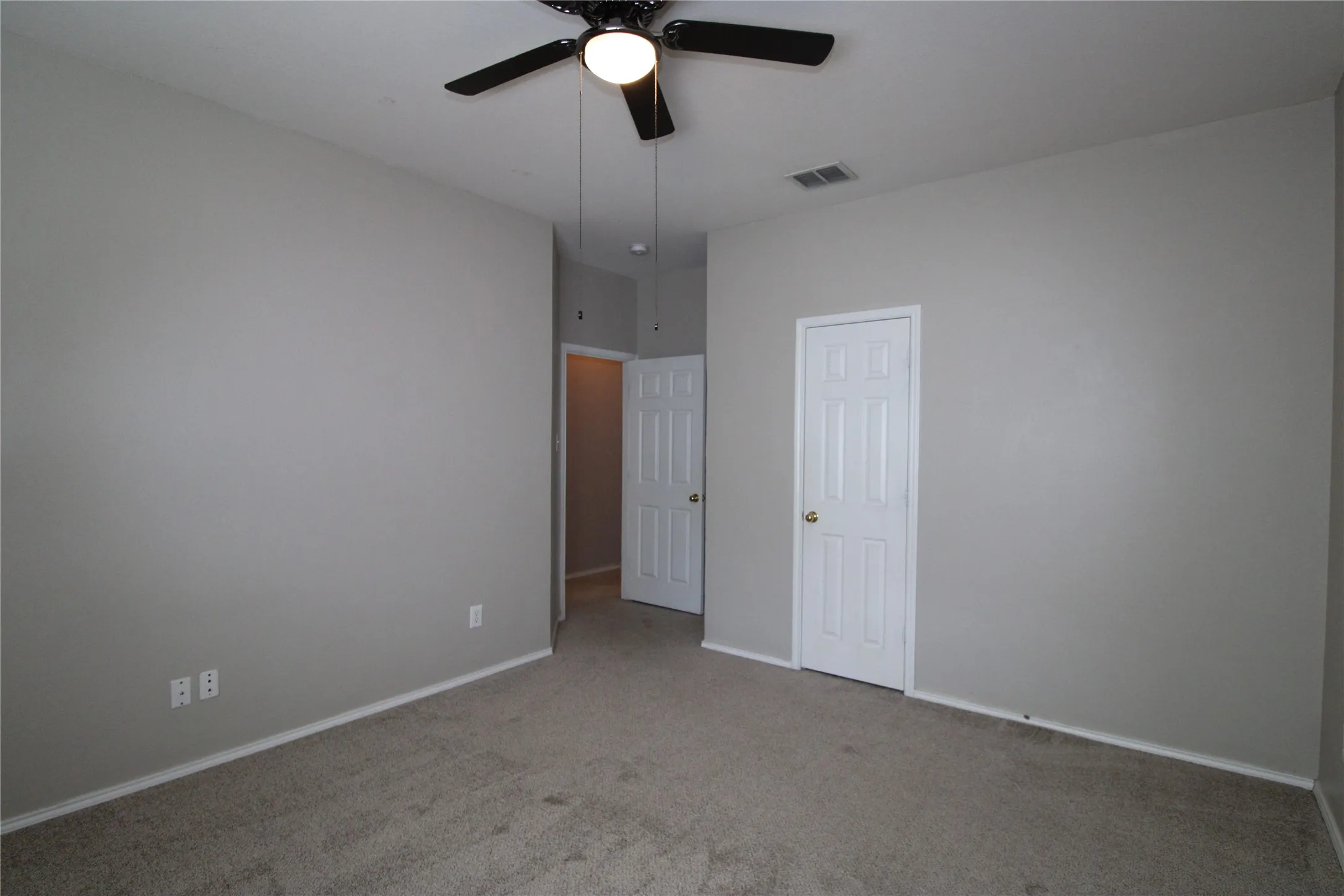 Neutral gray walls with white trim, a black ceiling fan, and gray carpeting