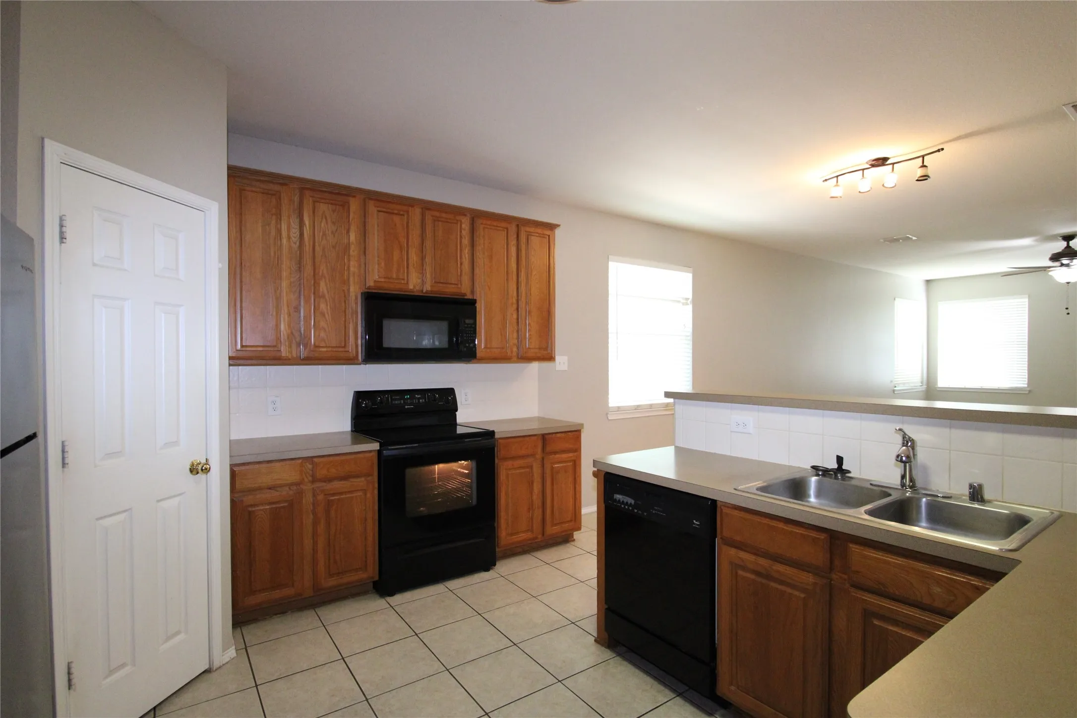 Kitchen featuring wood cabinetry, stainless steel double basin sink, black appliances, solid surface countertops, and tile flooring