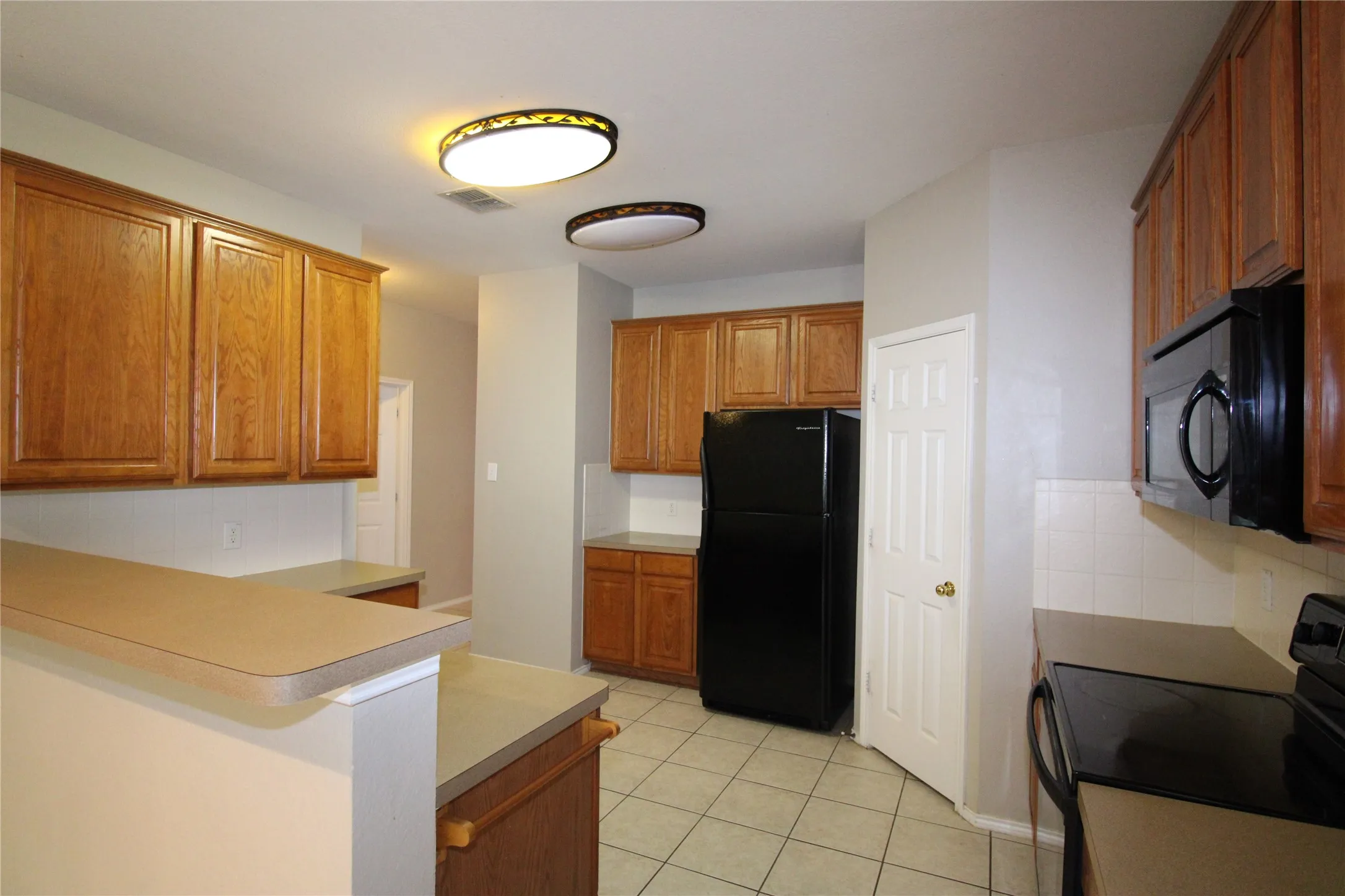 Kitchen featuring wood cabinetry, laminate countertops, tile flooring, and integrated black appliances