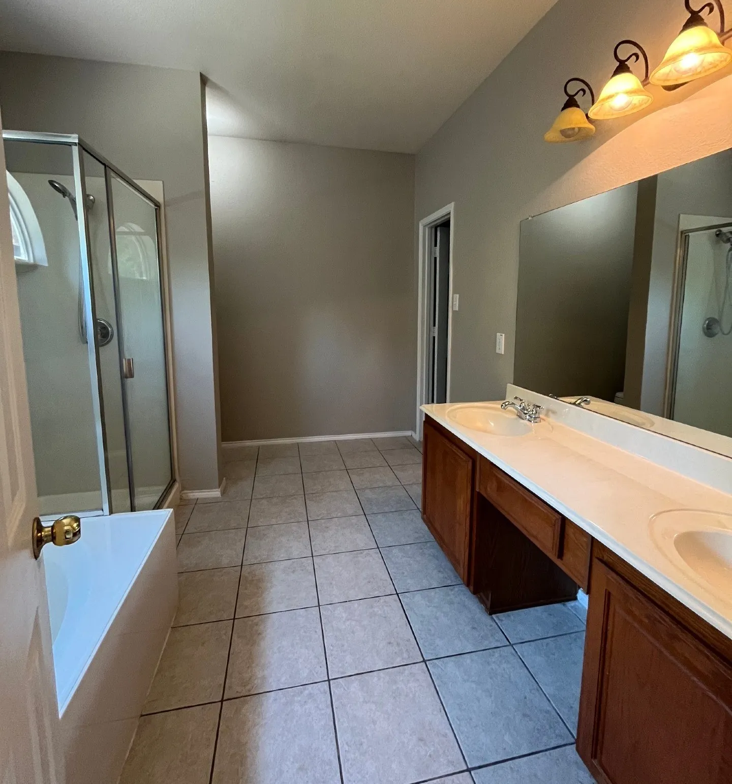 Dual vanity with integrated sinks, expansive counter space, wood-finish cabinetry, tile flooring, and a glass-enclosed shower
