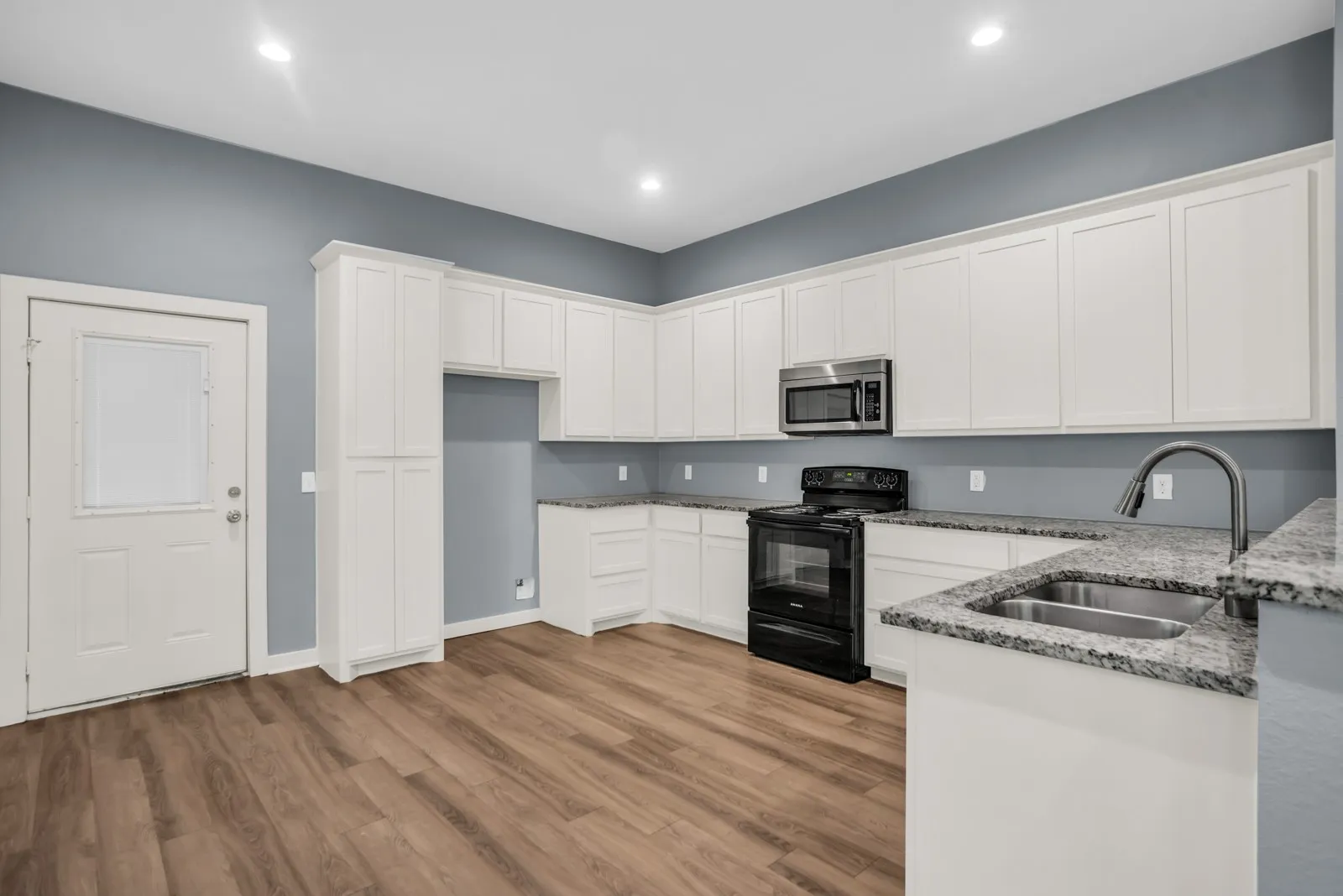 Kitchen featuring white cabinetry, wood-finish flooring, granite countertops, a stainless steel microwave, and a black range