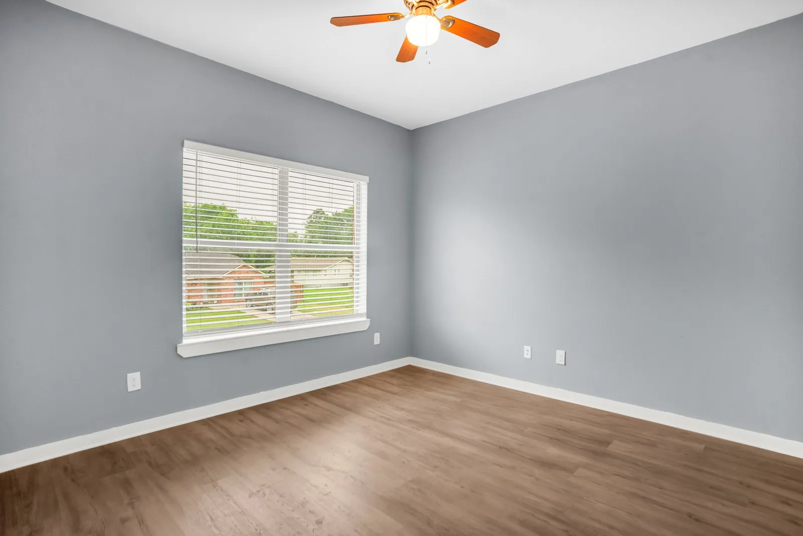 Spacious room featuring wood-finish flooring, a ceiling fan with integrated lighting, and a large window with blinds
