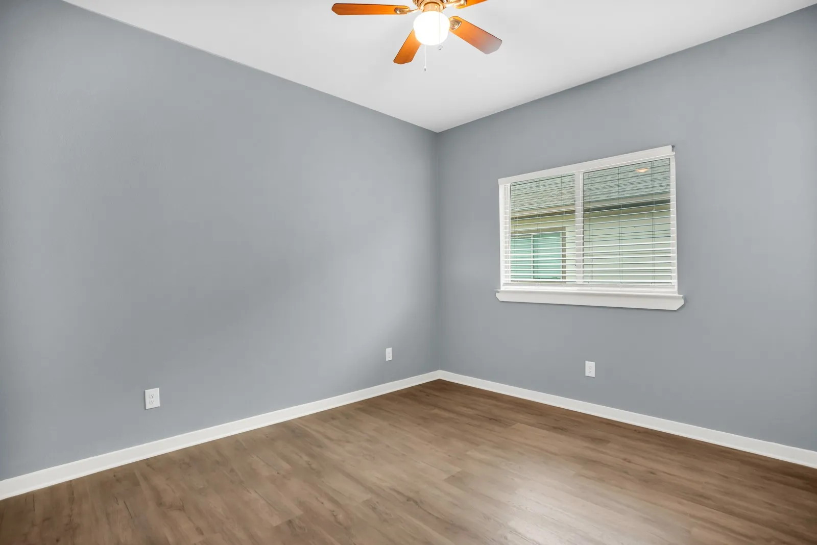Room featuring wood-finish flooring, a ceiling fan with integrated lighting, and a window with white blinds