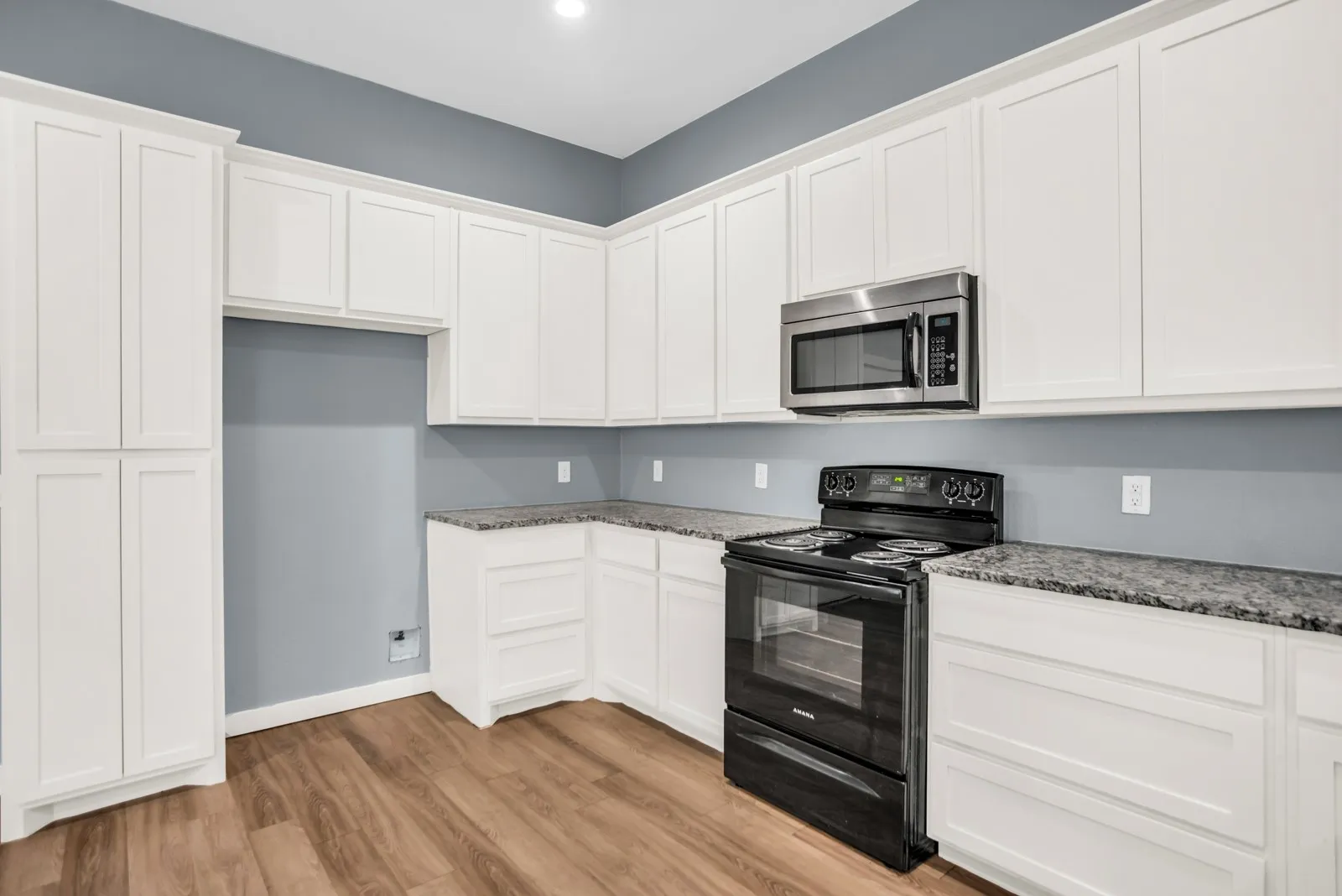 Kitchen featuring extensive white shaker cabinetry, speckled countertops, wood-finish flooring, a stainless steel microwave, and a black electric range