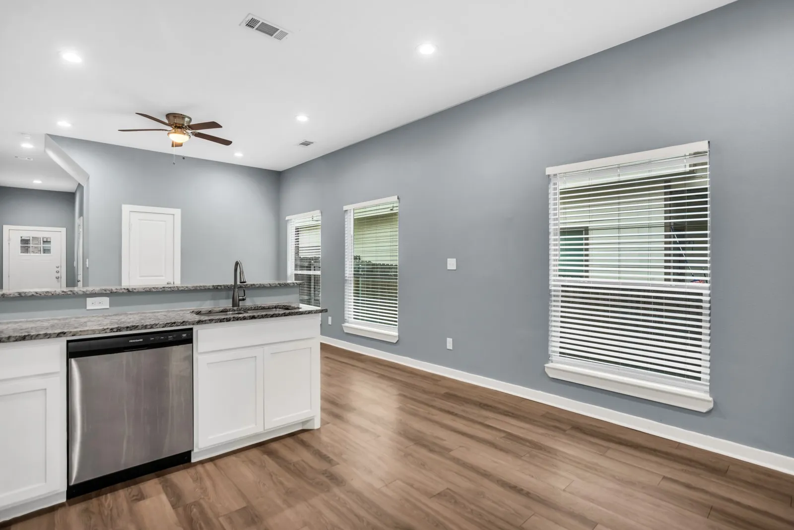 Kitchen island featuring a stainless steel dishwasher, undermount sink with a gooseneck faucet, white cabinetry, and a stone-finish countertop