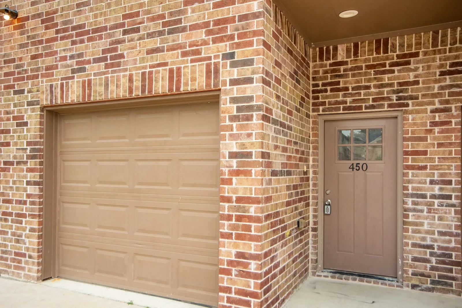 Multicolor brick exterior featuring a tan panel garage door and a complementary tan front entry door