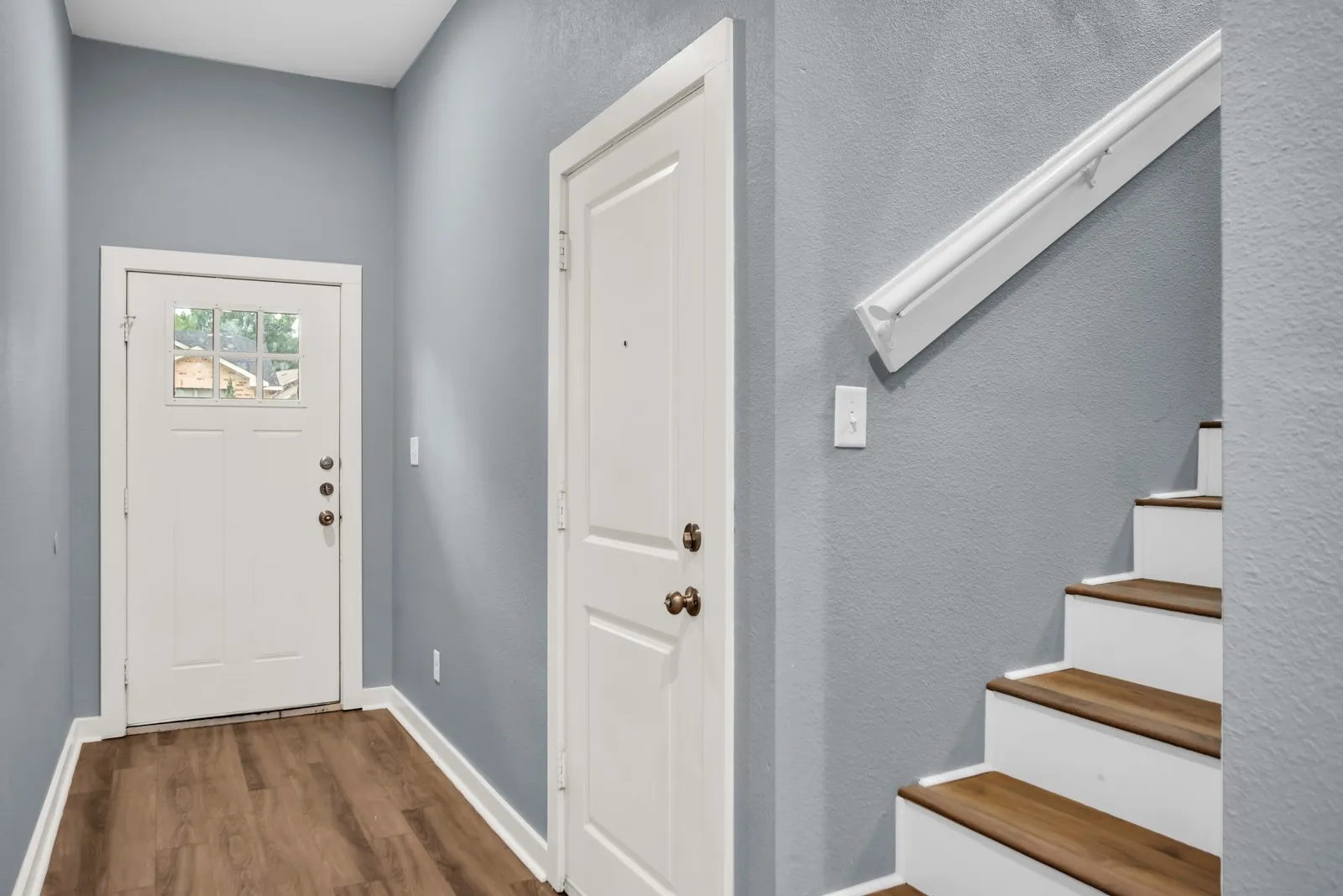 Entryway featuring wood-finish flooring, a white front door with multiple glass panes, and a white staircase with wood-finish treads and a white handrail