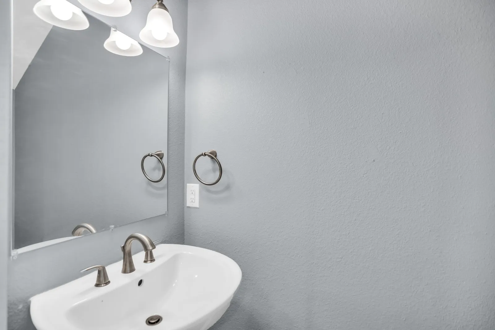 White pedestal sink with a brushed nickel faucet, framed by a rectangular mirror