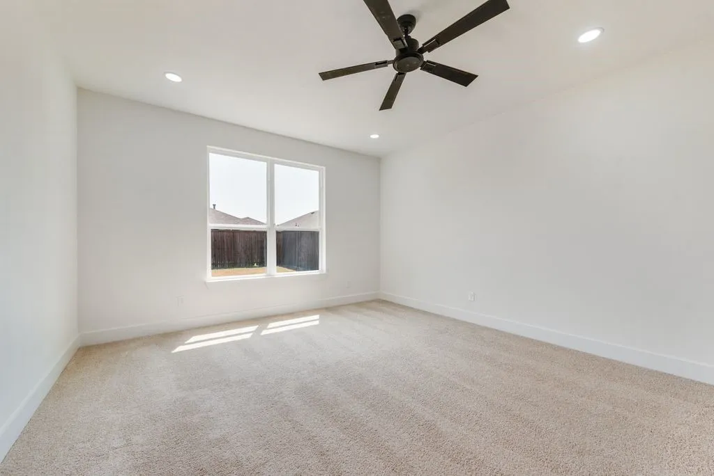 Neutral-toned carpeting, ample natural light from a multi-pane window, recessed lighting, and a ceiling fan with integrated lighting