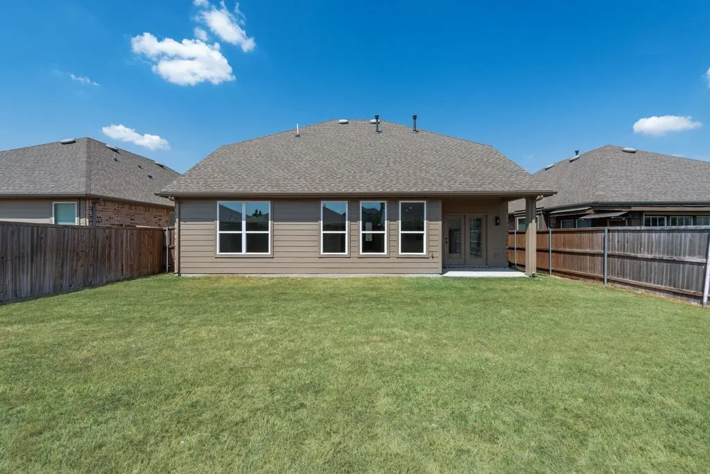 Expansive grassy backyard featuring a partial wood fence, a concrete patio, and a covered patio area with dual-pane glass doors