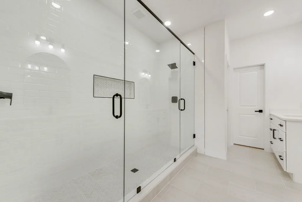 Glass-enclosed shower with matte black hardware, subway tile surround, and recessed shelving