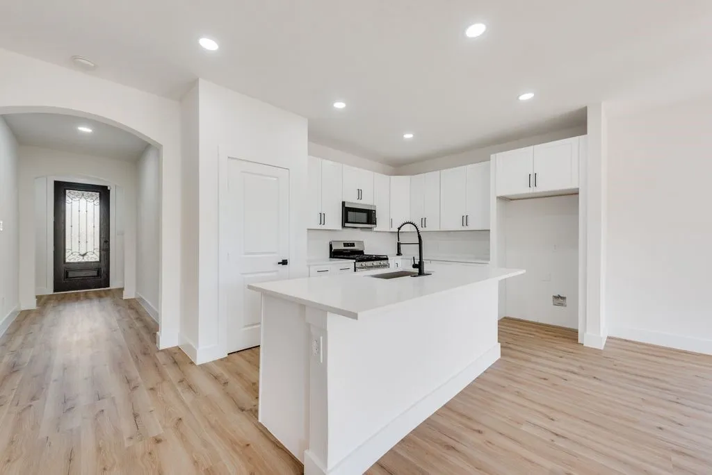 Modern kitchen featuring a central island with a sink, white cabinetry, integrated microwave, and wood-finish flooring