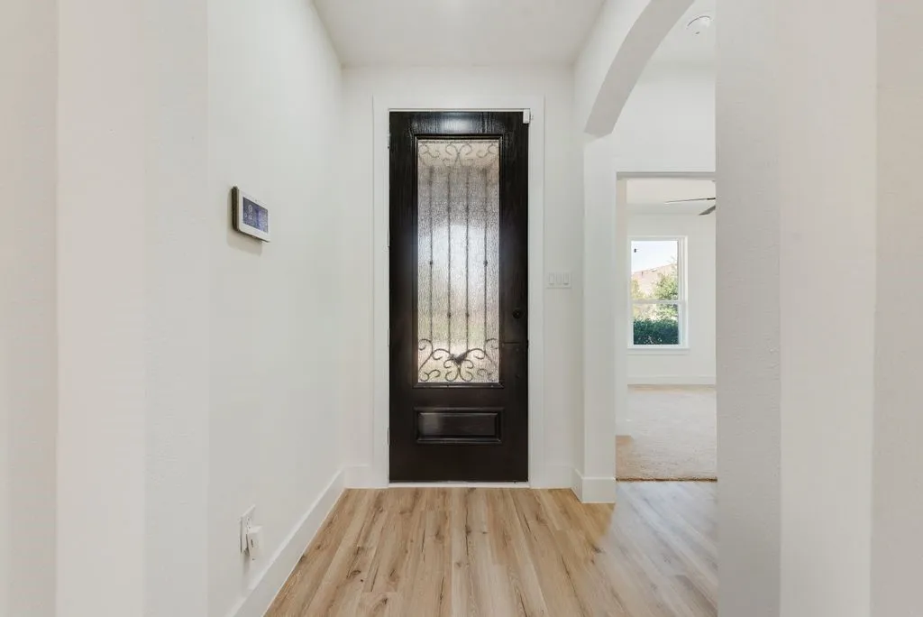 Wood-finish flooring, dark wood entry door with ornate glass insert, white painted walls, and an arched doorway